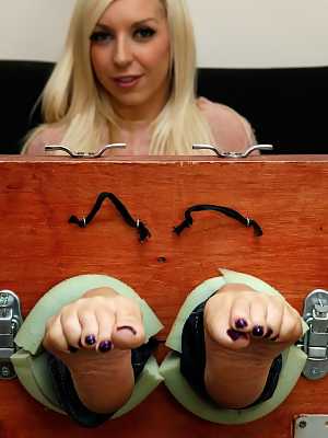 Blonde chick Alex Adams wiggles her toes while her feet are in stocks