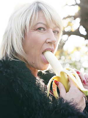 Mature blonde woman eats a banana before a gangbang in the countryside