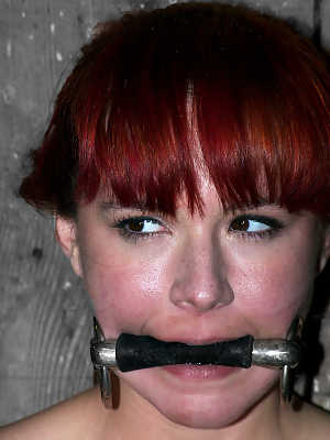 Naked redhead has her nipples and clit affixed with clamps while restrained