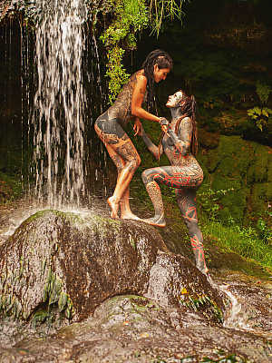 Heavily tattooed lesbians hold each other while totally naked on a bridge