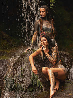 Heavily tattooed lesbians hold each other while totally naked on a bridge