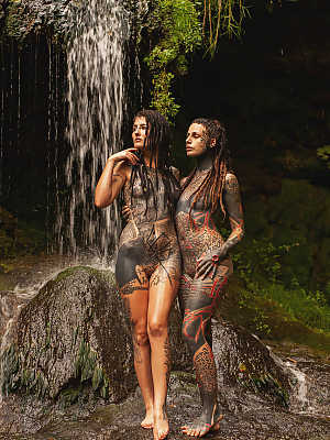 Heavily tattooed lesbians hold each other while totally naked on a bridge