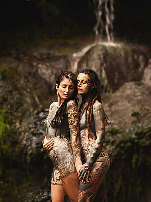 Heavily tattooed lesbians hold each other while totally naked on a bridge