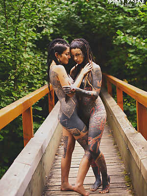 Heavily tattooed lesbians hold each other while totally naked on a bridge