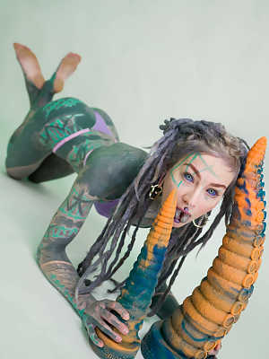 Heavily tattooed girl Anuskatzz holds a couple of taintacle toys in the nude