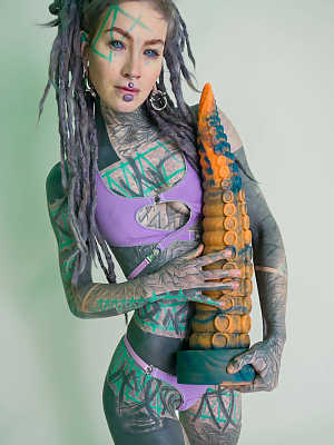 Heavily tattooed girl Anuskatzz holds a couple of taintacle toys in the nude