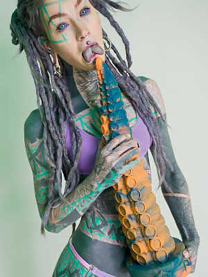 Heavily tattooed girl Anuskatzz holds a couple of taintacle toys in the nude