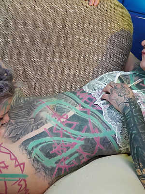 Heavily tattooed girls engage in anal play during GGB sex on a sofa