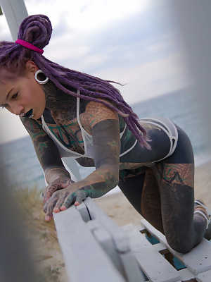 Heavily tattooed girl models a bikini in heels on a beach patio