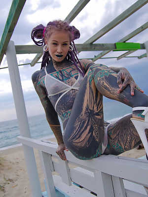 Heavily tattooed girl models a bikini in heels on a beach patio