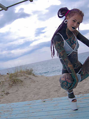 Heavily tattooed girl models a bikini in heels on a beach patio