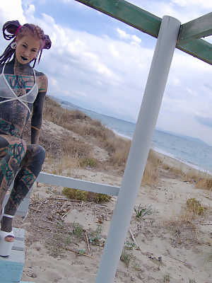 Heavily tattooed girl models a bikini in heels on a beach patio