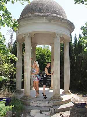 Two oiled lesbian babes use a double-ended dildo together in the gazebo ruins