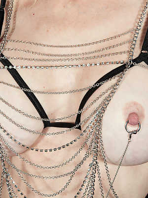 Mature lady Cammille Austin shows off her pierced nipples in chains and thong