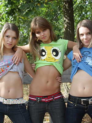 Three young looking girls gets naked on a wooden bench in the countryside