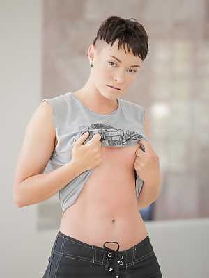 Short haired dyke Jiz Lee strips for nude poses against a cinder block wall