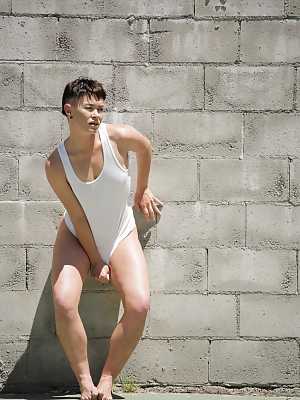 Short haired dyke Jiz Lee strips for nude poses against a cinder block wall