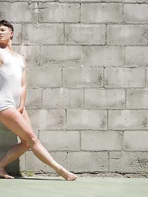 Short haired dyke Jiz Lee strips for nude poses against a cinder block wall